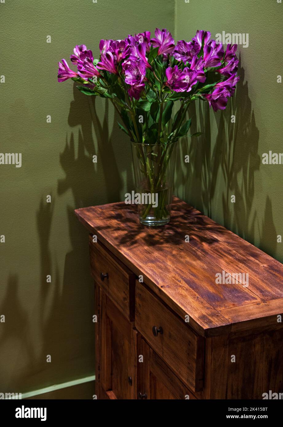 Lily flowers bouquet on vintage wooden chest of drawers in green painted room. Rustic interior ideas concept. Lifestyle background. Stock Photo