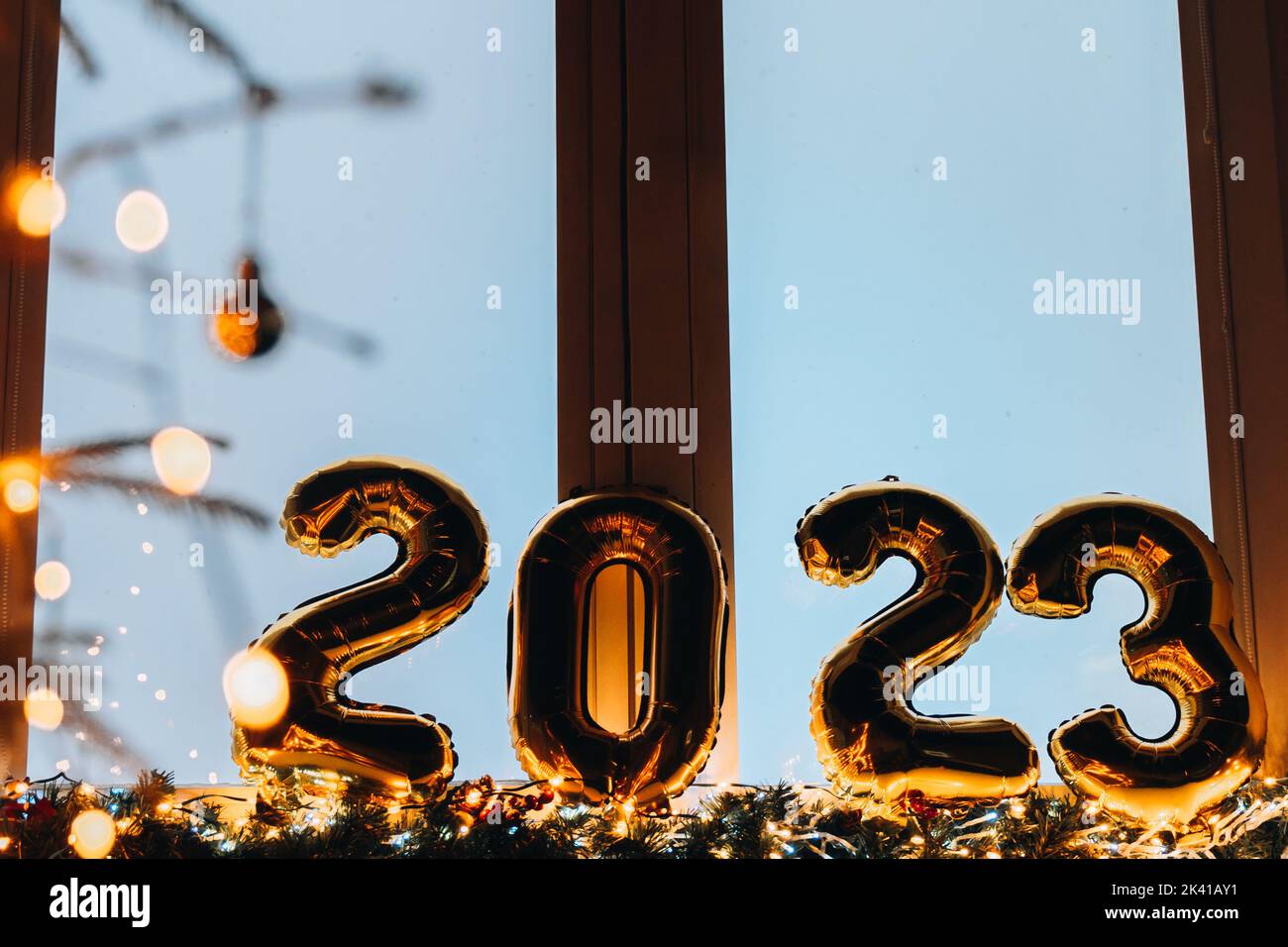2023 golden foil balloons on blue window sill. Celebrating holidays at home, festive decor concept. Happy New Year 2023. close-up numbers of year 2023 Stock Photo
