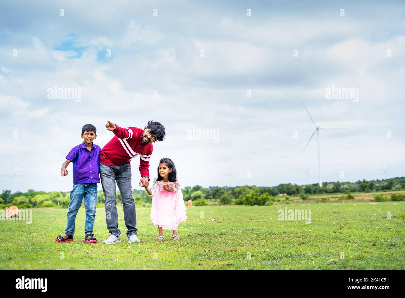 Happy indian father enjoying weekend with kid and showing wind fan at power station - concept of weekend, bonding and renewable energy. Stock Photo
