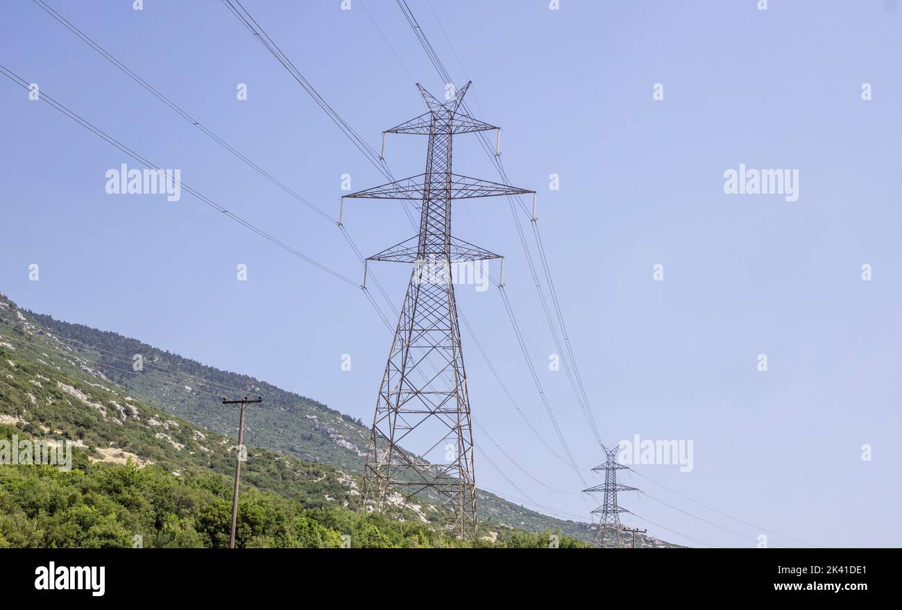 High voltage electric pylons at Greek forest mountain background. Metal pole with power transformer line. Energy transmission concept. Stock Photo