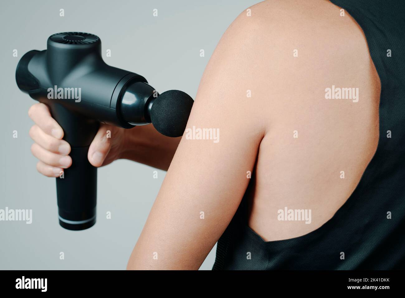 closeup of a young caucasian man, wearing sports clothes, using a massage gun to massage the muscles of his arm Stock Photo