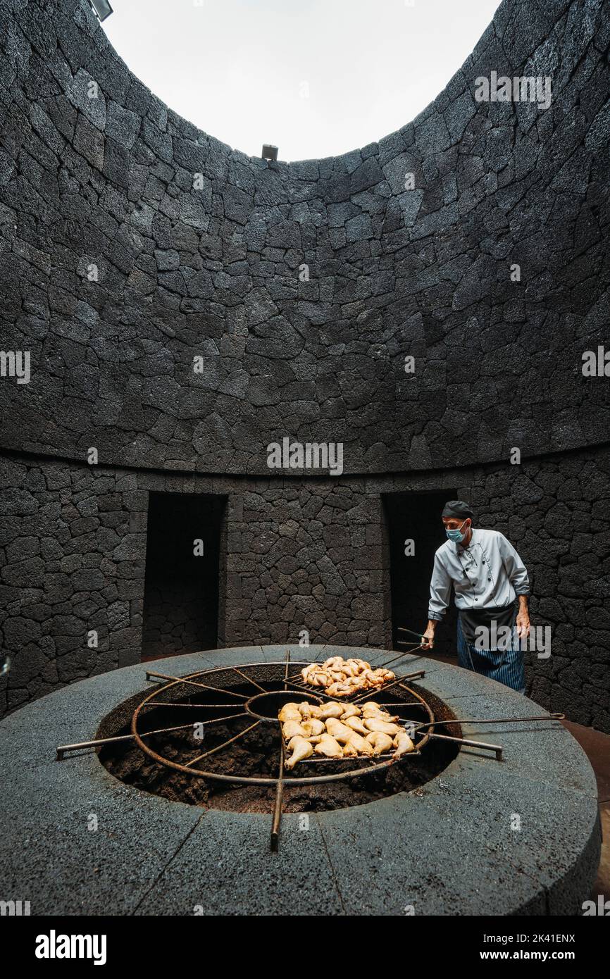 Timanfaya National Park, Spain - April 24, 2022: Cook grilling chicken on volcanic heat in El Diablo restaurant Stock Photo