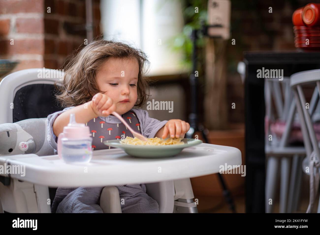 portrait caucasian baby girl about 2 years old in bib eating pasta from