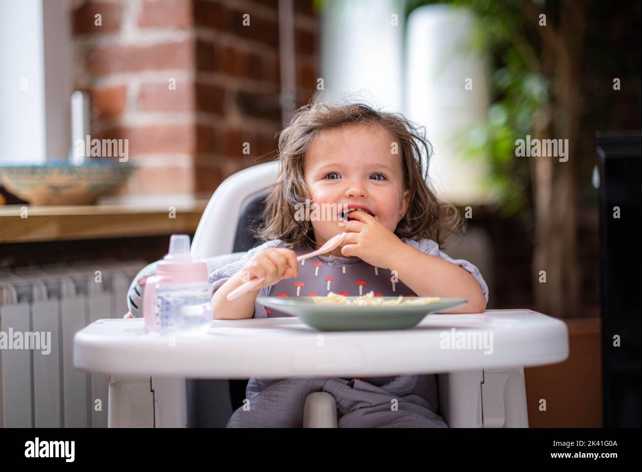portrait caucasian baby girl about 2 years old in bib eating pasta from