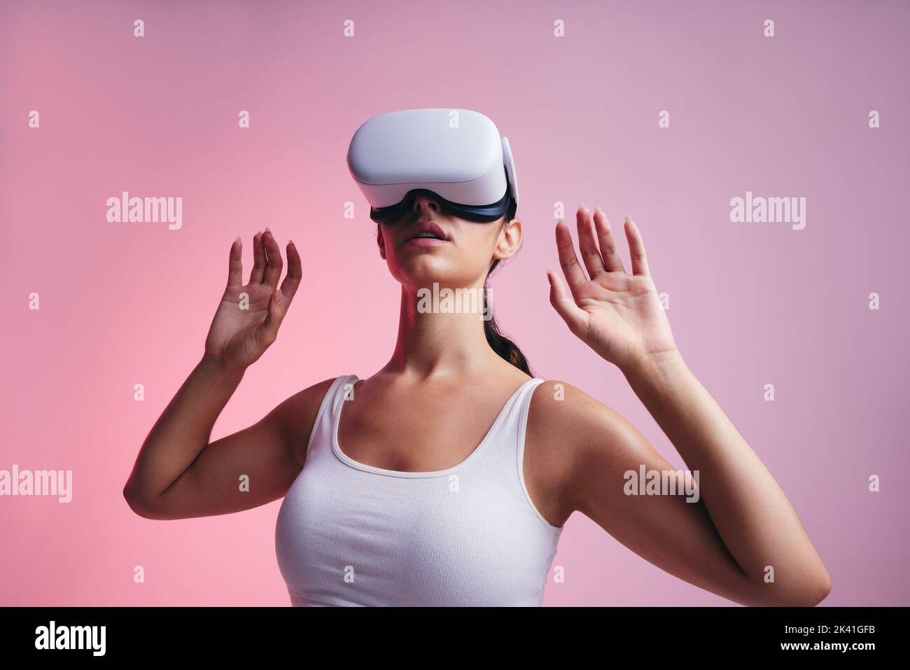 Looking around the metaverse. Young woman exploring immersive technology in a studio. Young woman entering a 3D game while wearing a virtual reality h Stock Photo