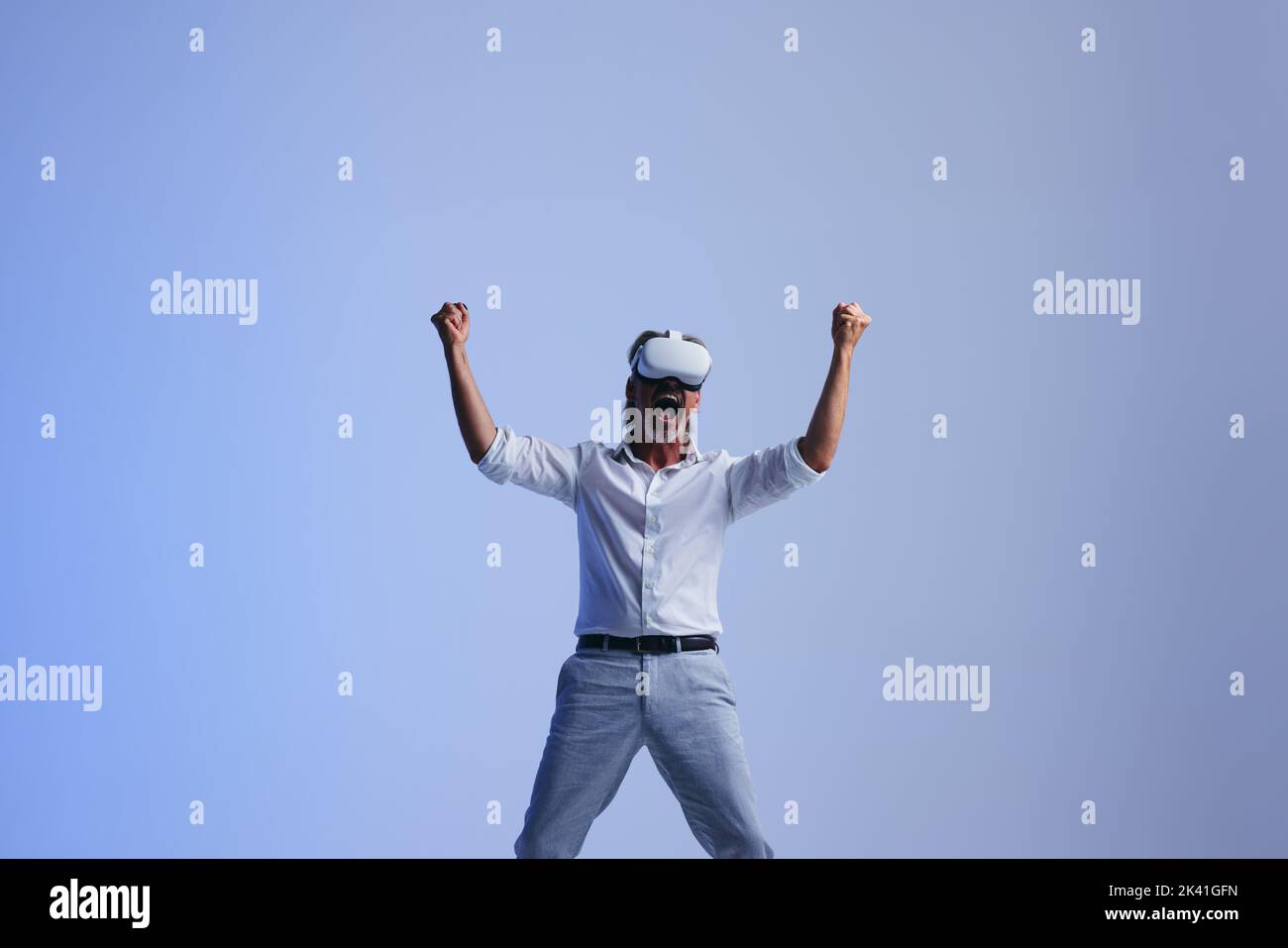 Successful businessman celebrating his victory in the metaverse. Mature businessman cheering while wearing a virtual reality headset. Businessman work Stock Photo