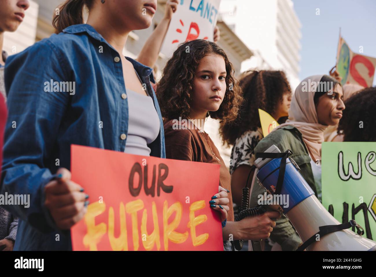 Teenage girl holding a megaphone while marching for climate justice with a group of demonstrators. Multicultural youth activists protesting against gl Stock Photo