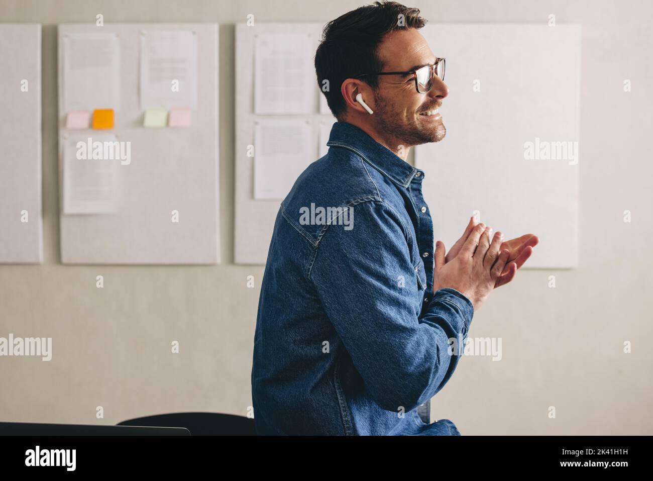 Cheerful businessman having a conference call using earbuds. Happy young businessman smiling while communicating with his team. Businessman with glass Stock Photo