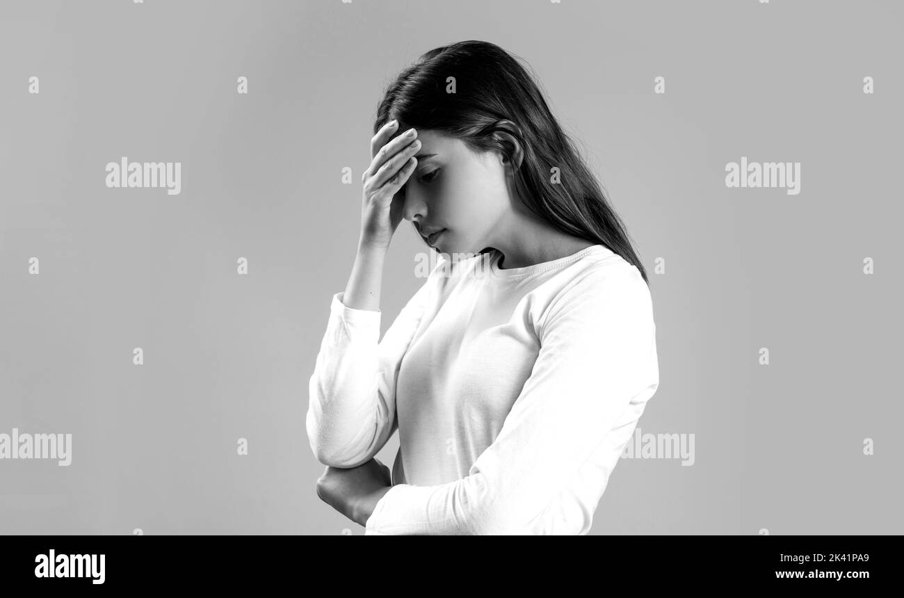 Woman with hard headache holding hands on head. Brunette woman touching her temples feeling stress, on gray background. Black and white Stock Photo
