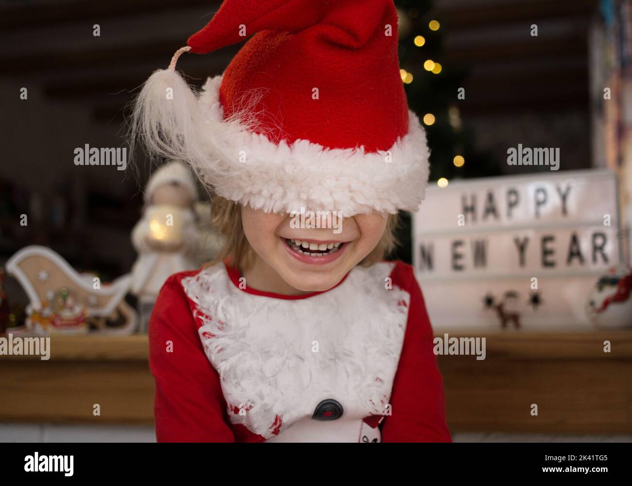 smiling happy child in a red santa hat, hid, pulling the hat over his eyes. The kid is waiting for a miracle. Christmas, New Year, merry family winter Stock Photo