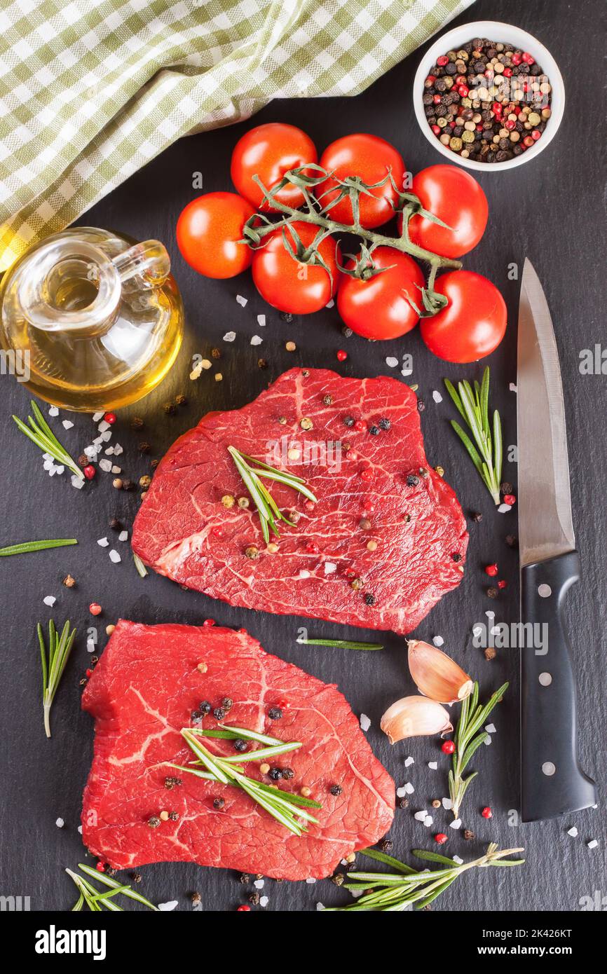 Raw steak with rosemary, salt and pepper on black slate background