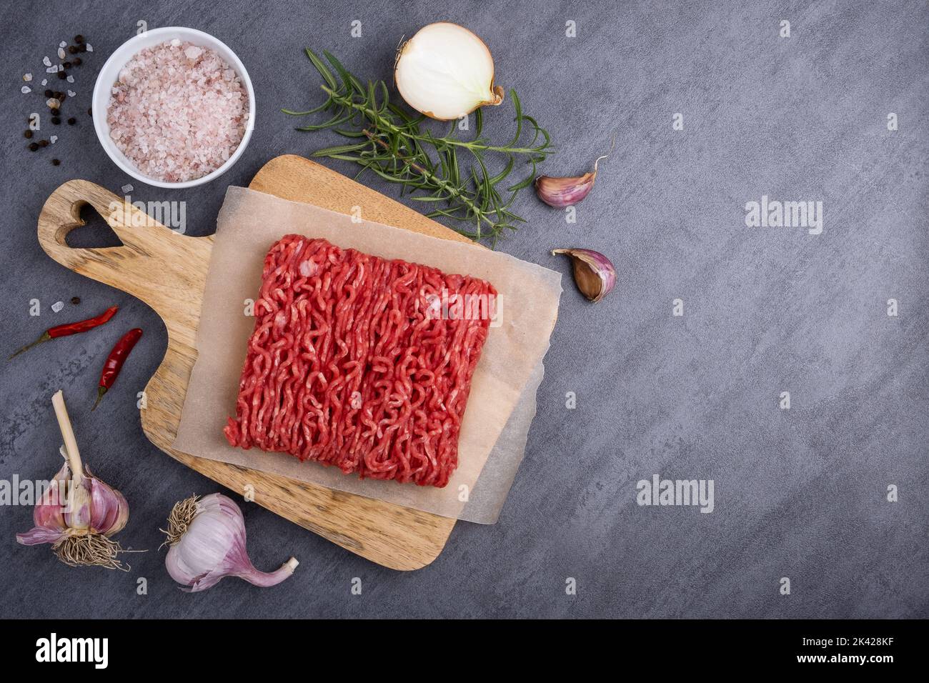 Minced meat lies on a cutting board surrounded by cooking ingredients. Stock Photo