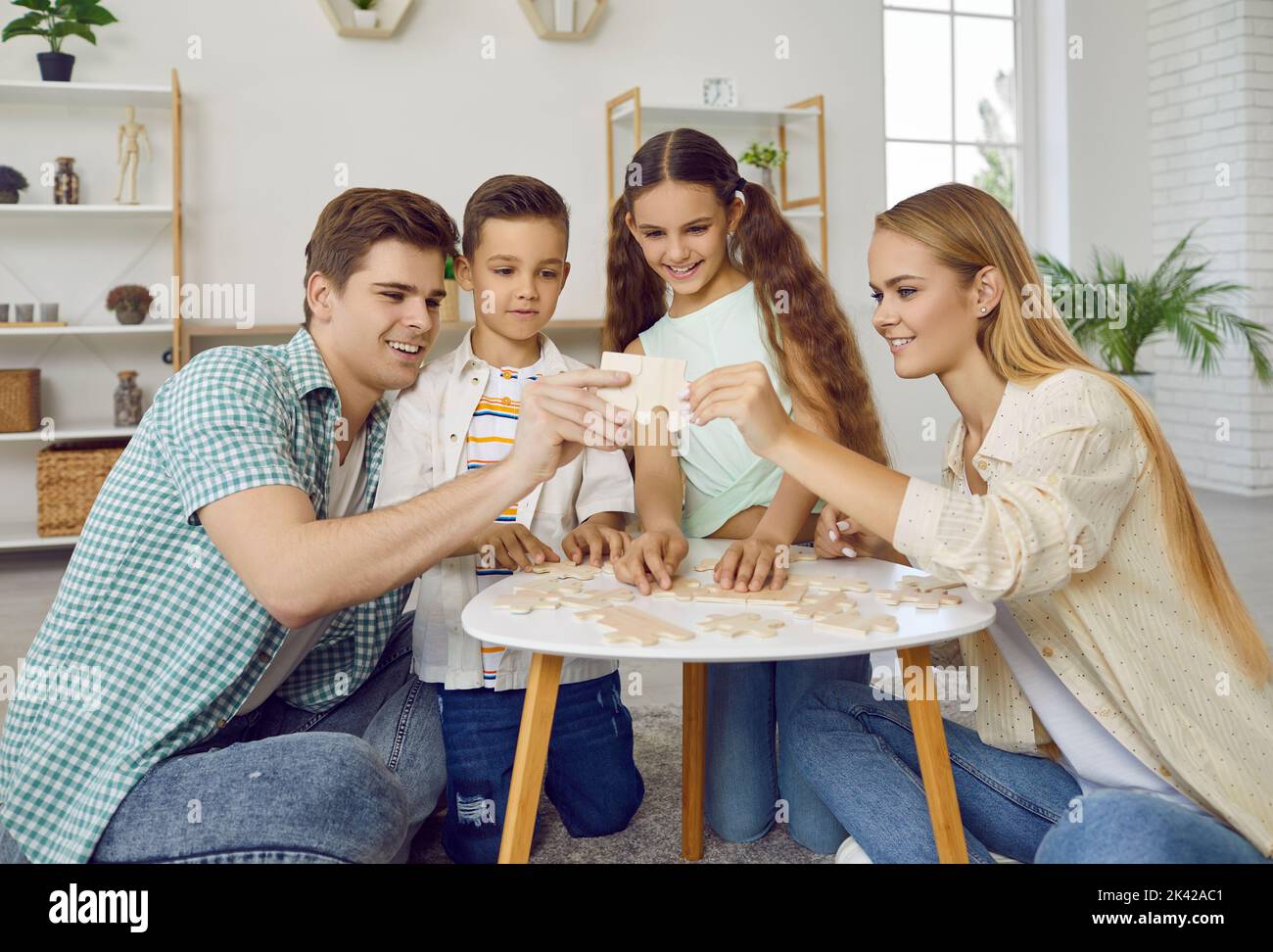 Friendly family with two children are playing puzzles at table sitting on floor at home in weekend. Stock Photo