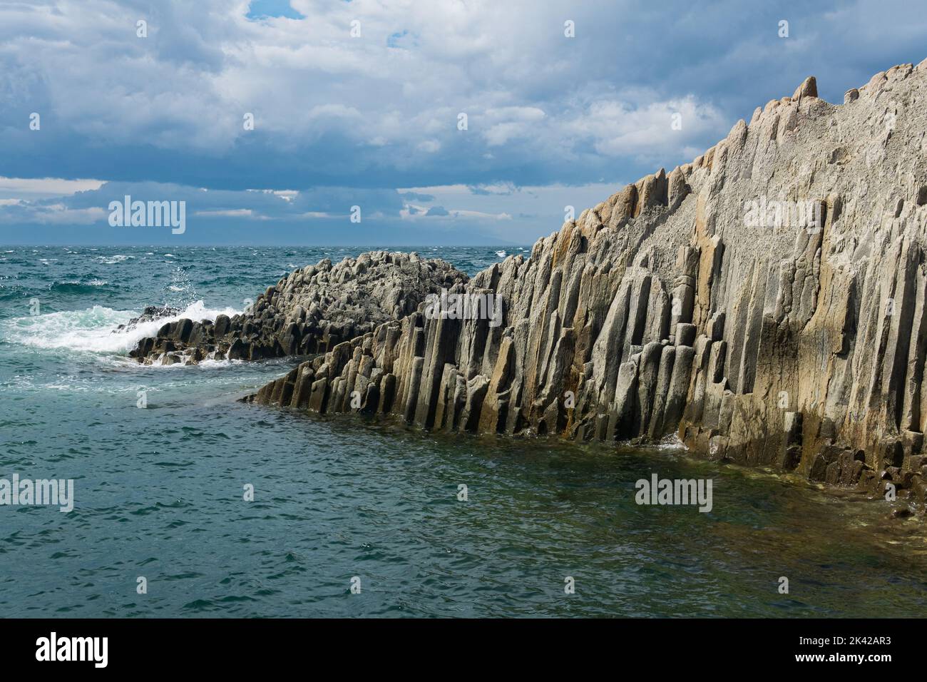 rocky seashore formed by columnar basalt against the surf, coastal landscape of the Kuril Islands Stock Photo