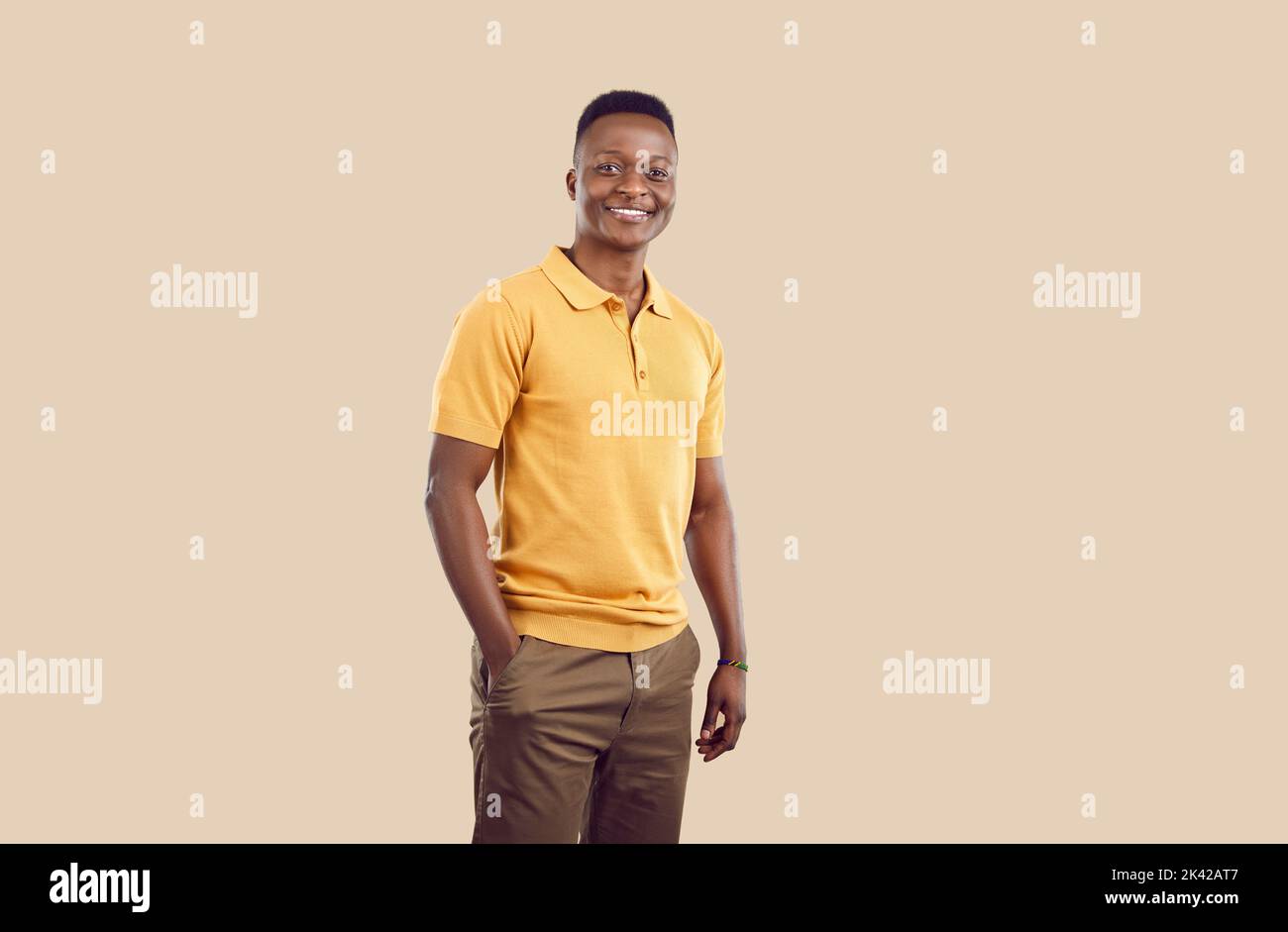 Young smiling African American man posing with one hand in pocket pants stands on beige background Stock Photo