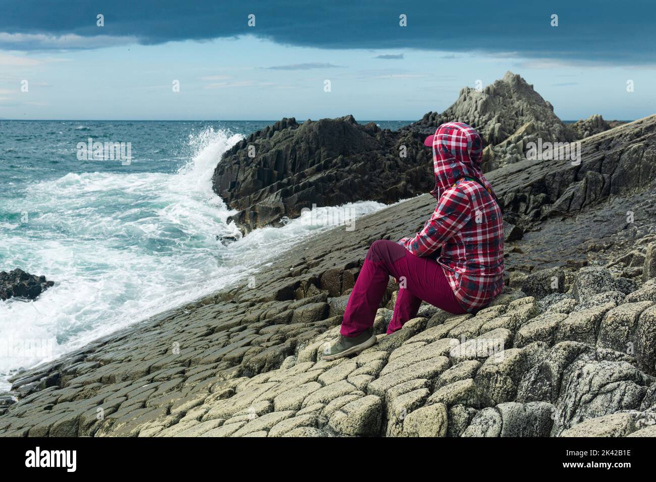 traveler sits on the shore of a stormy sea, on a natural pavement made of columnar granite Stock Photo
