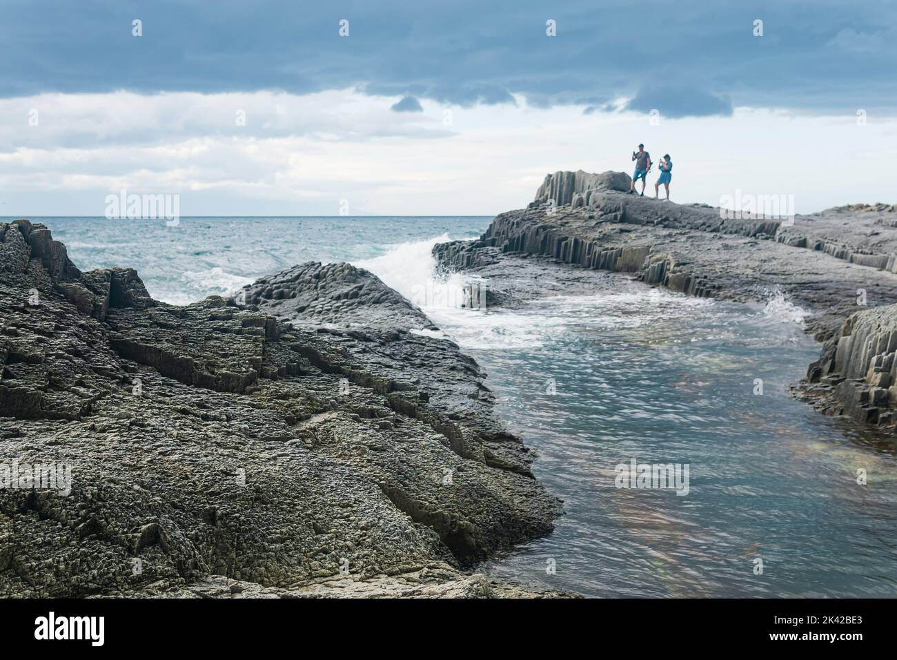 Kunashir, Russia - Juiy 31, 2022: coastal seascape with beautiful columnar basalt rocks at low tide, people is seen in the distance in blur Stock Photo