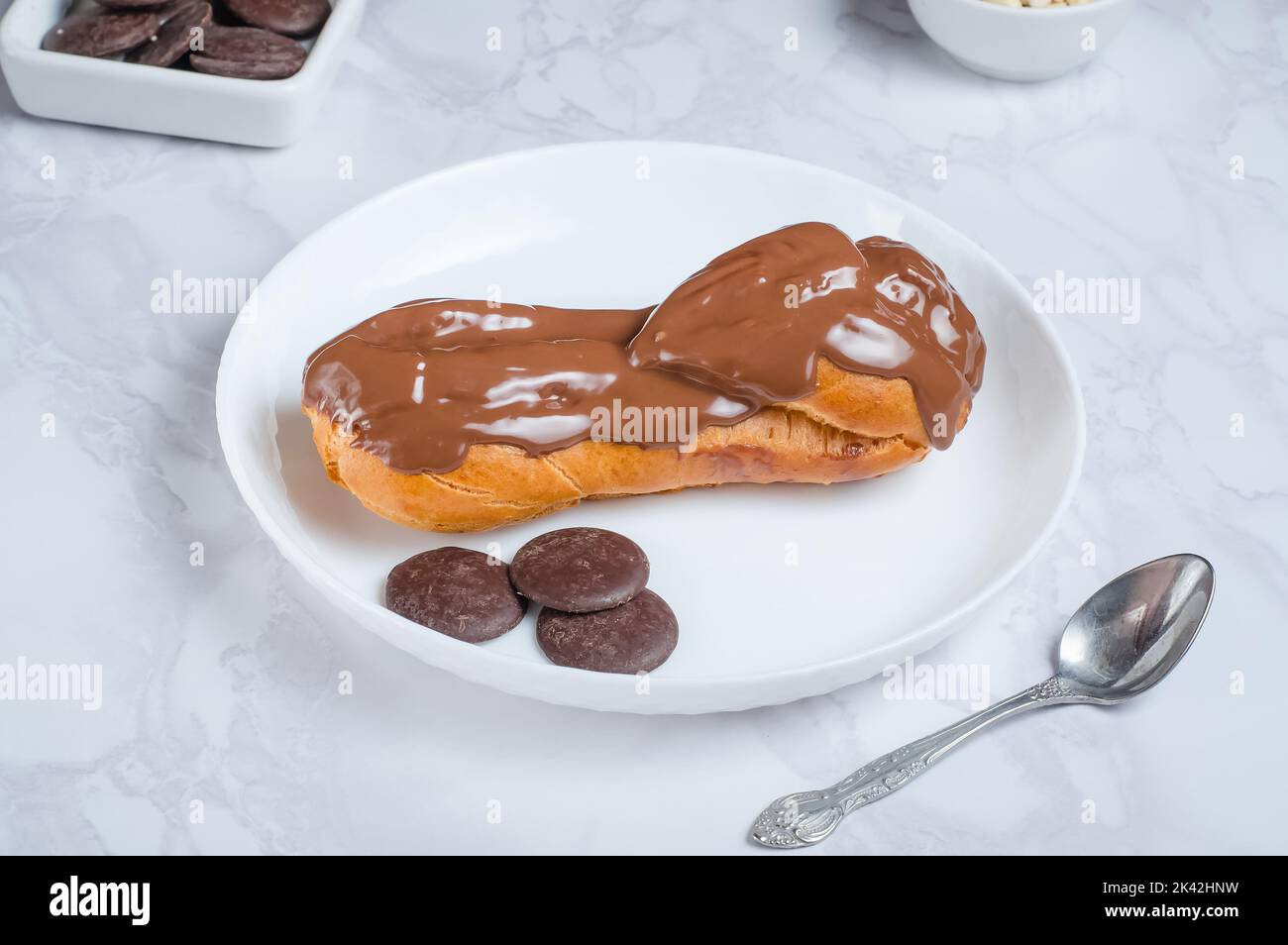 Appetizing eclair covered with chocolate on a white serving plate on a gray background Stock Photo