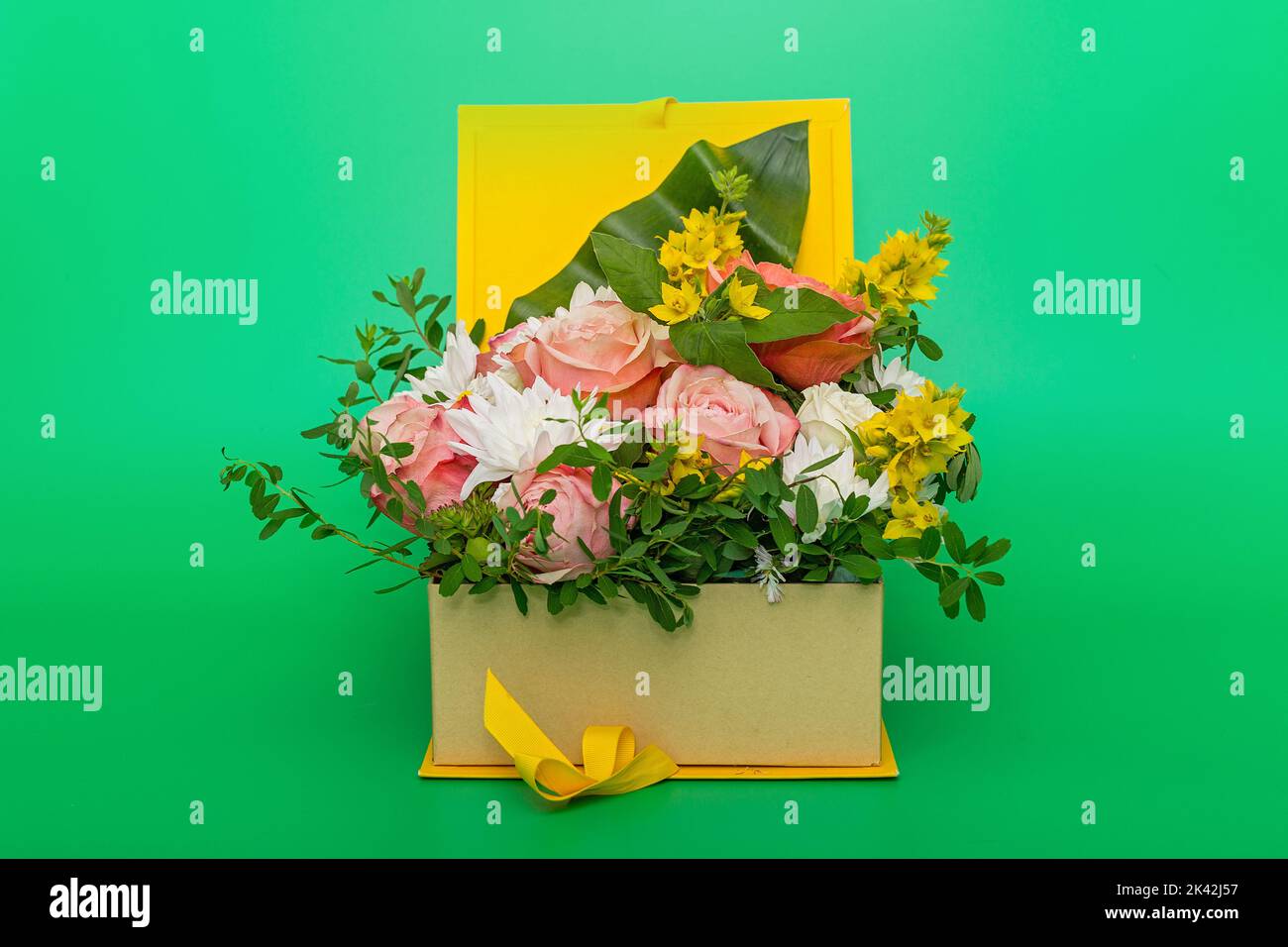 Original flower arrangement in a yellow gift box, on a green background Stock Photo