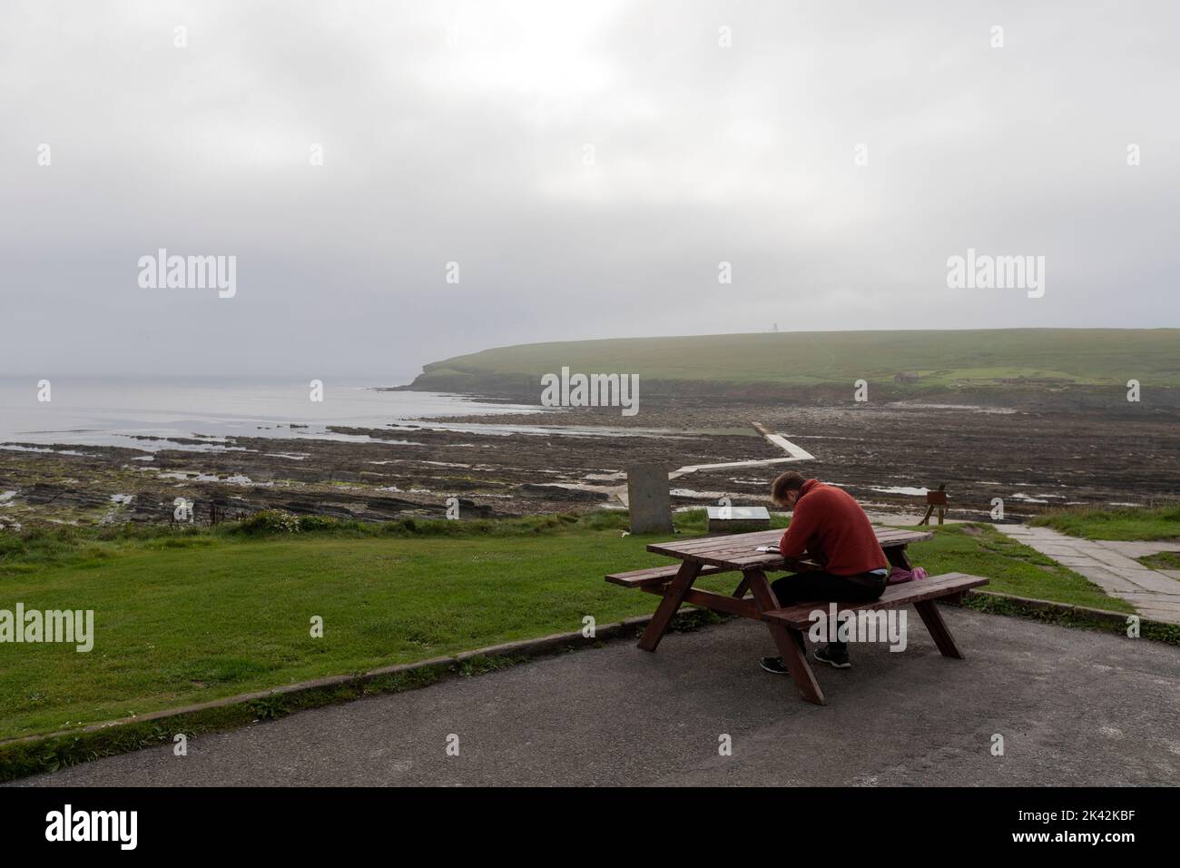 Tourist in a picnic table and the Concrete pathway to the island Brough of Birsay, The Mainland of Orkney, Scotland, UK Stock Photo