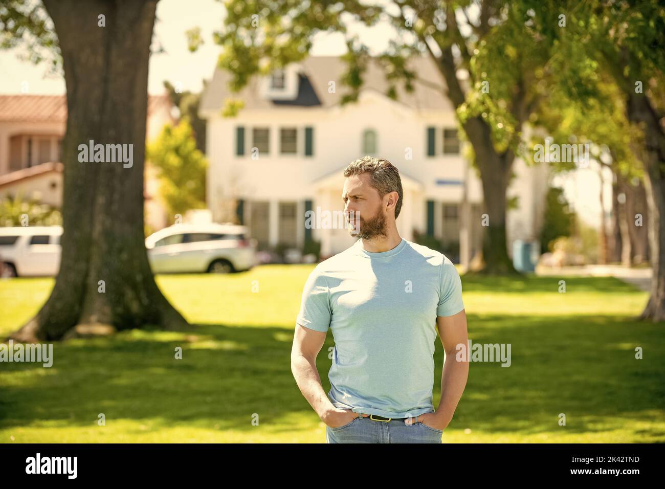 serious unshaven guy standing near new house, real estate Stock Photo