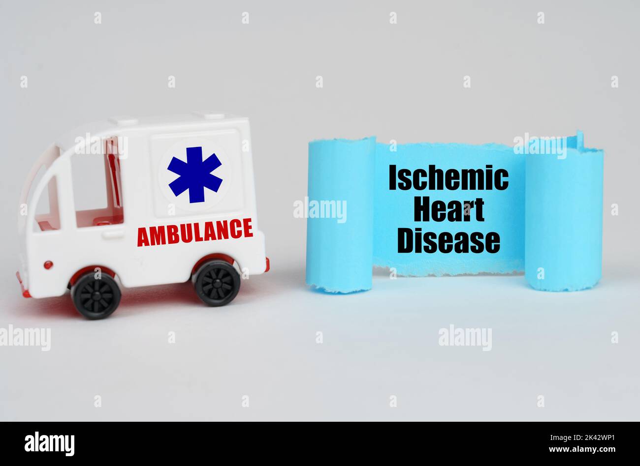 Medical concept. On a white surface, an ambulance and a blue paper sign with the inscription - Ischemic Heart Disease Stock Photo