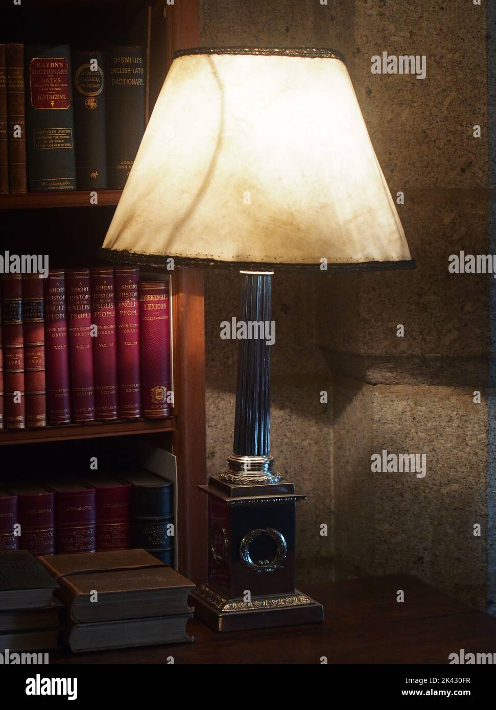 A large, heavy based, table lamp, lighting up a bookshelf of books