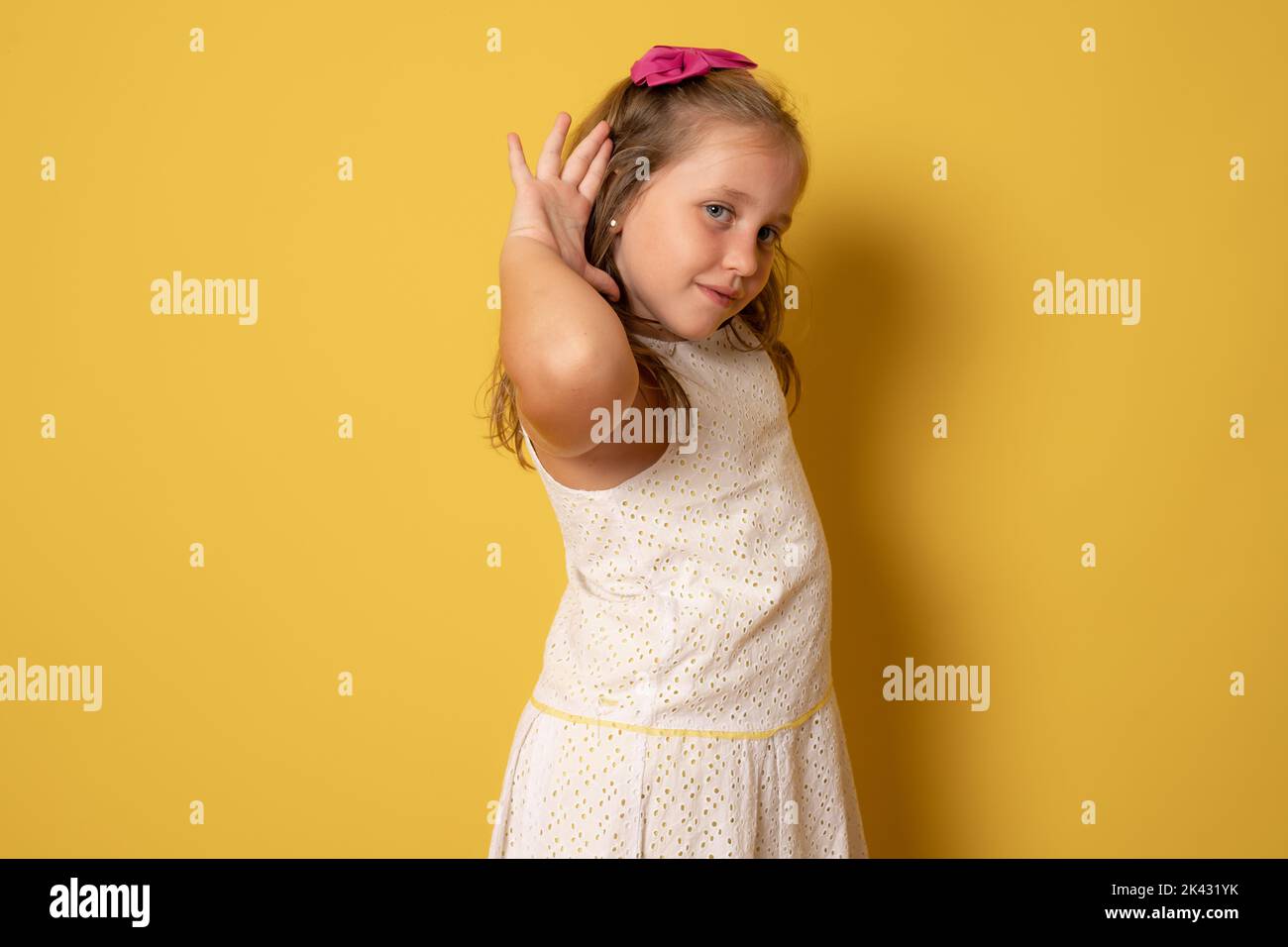 Little curious nosy kid child girl 6-7 years old try hear you overhear listen intently isolated on plain pastel light yellow background. Mother's Day Stock Photo