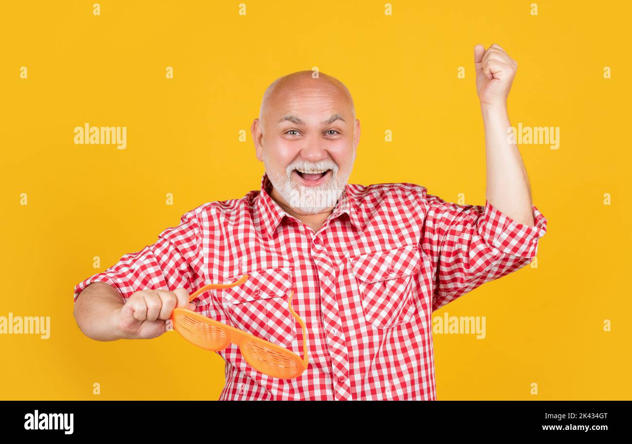 cheerful old man in checkered shirt with party glasses on yellow background Stock Photo