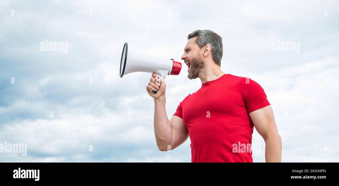 man in red shirt shout in loudspeaker on sky background Stock Photo