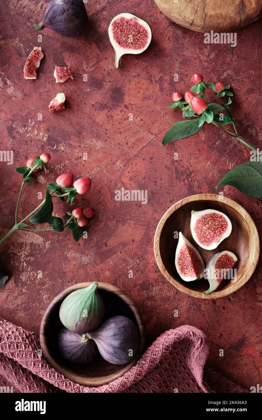 Panoramic banner Autumntime background with fresh halved fig fruits. Red hypericum berries with green leaves on dark brown background. Stock Photo