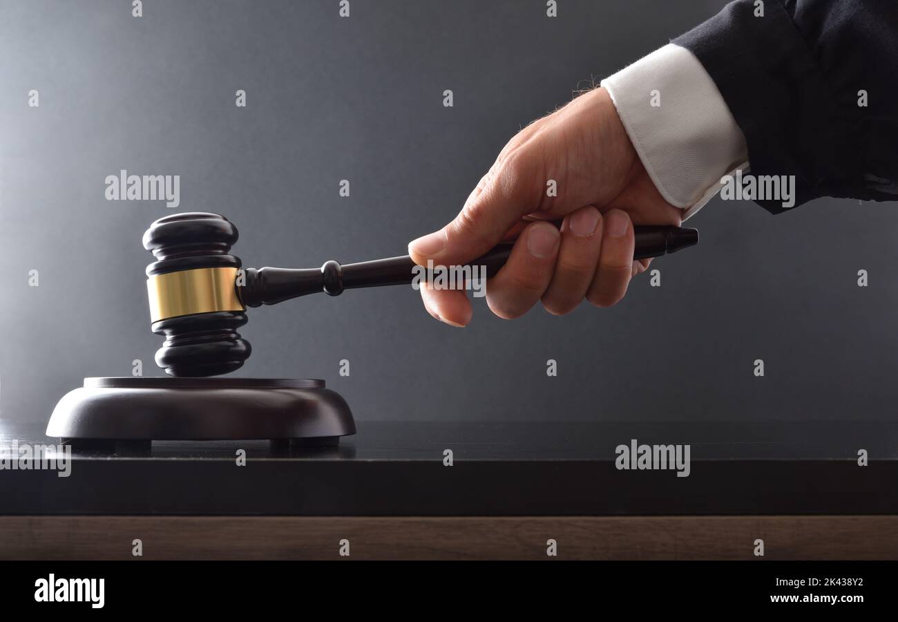 Hand striking on wooden base with judge's mallet on black table and black isolated background.  Front view. Stock Photo