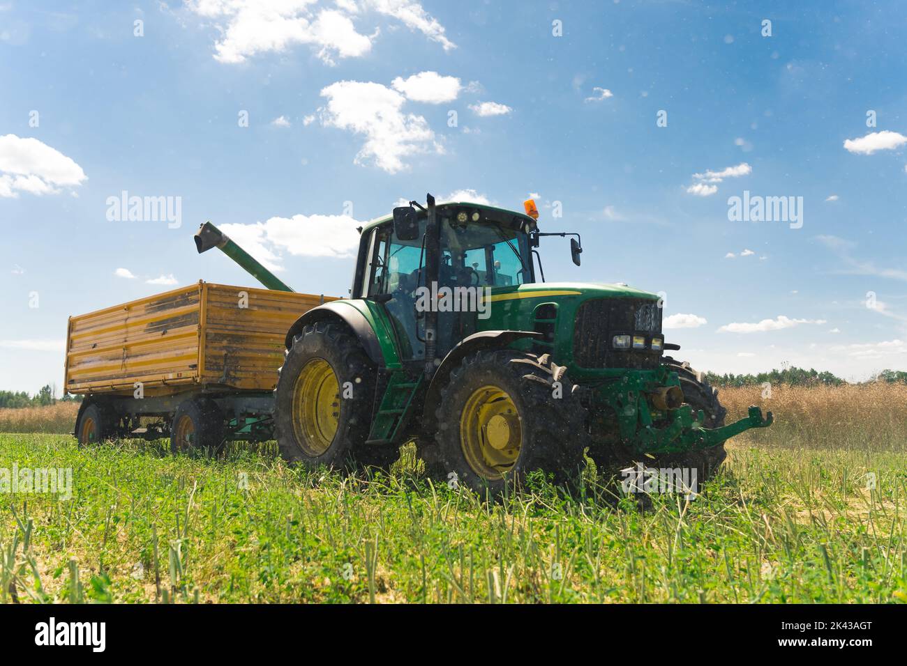 Summertime harvesting. Working in a field. Countryside concept. Full-length photo of professional giant tractor and yellow agriculture trailer. High quality photo Stock Photo