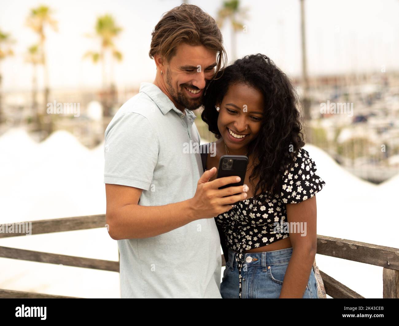 Diverse couple of happy heterosexual lovers looking at smartphone in a city on vacation Stock Photo