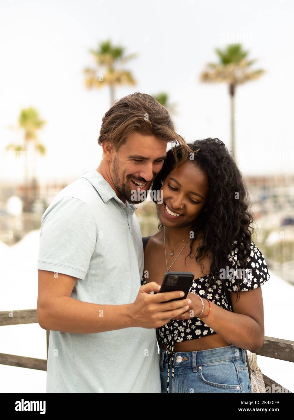 Diverse couple of happy heterosexual lovers looking at smartphone in a city on vacation Stock Photo