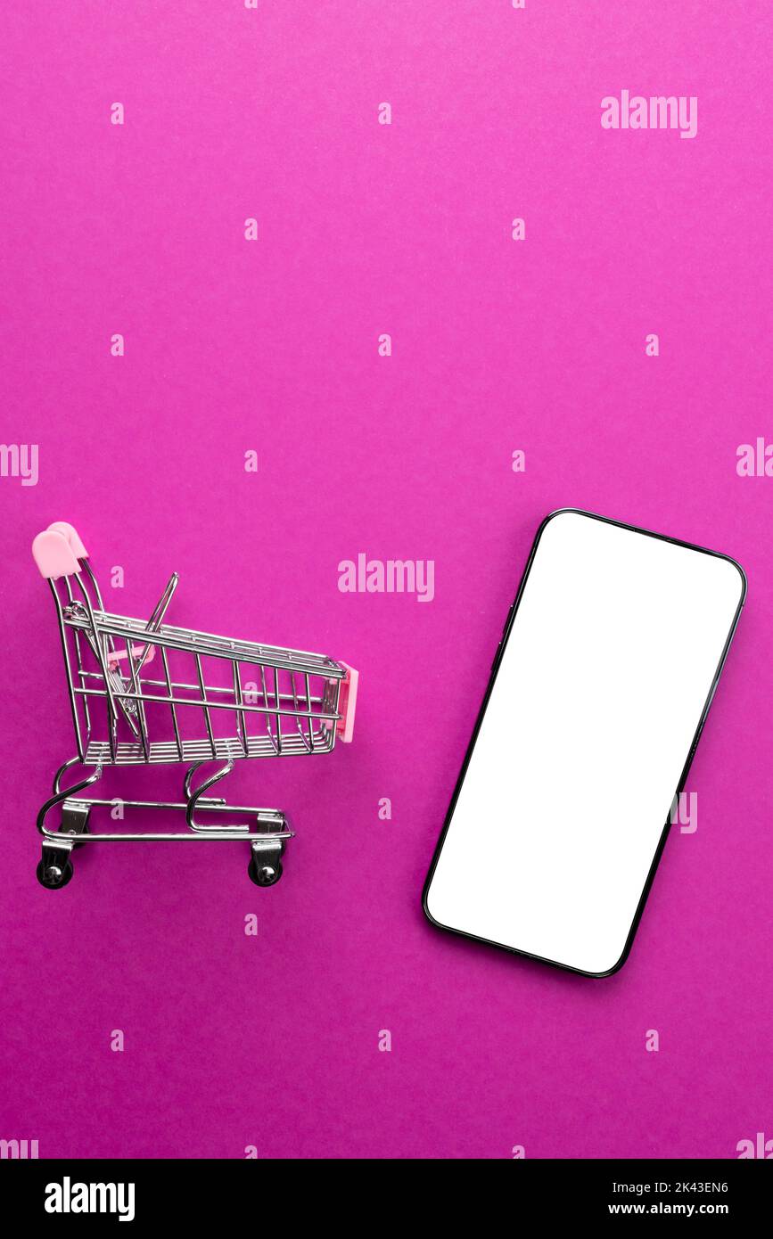 Composition of shopping cart and smartphone with copy space on pink ...
