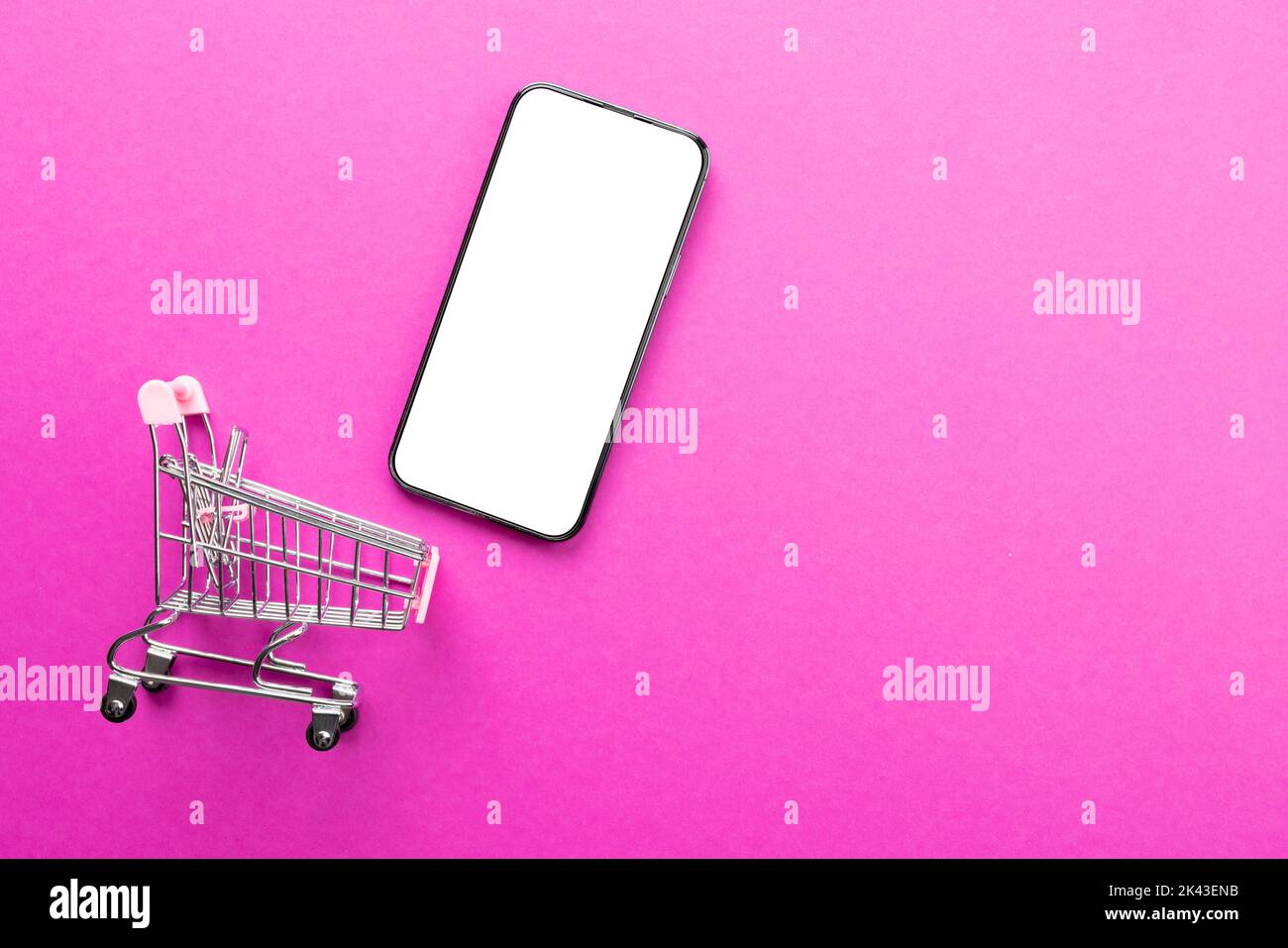 Composition of shopping cart and smartphone with copy space on pink ...