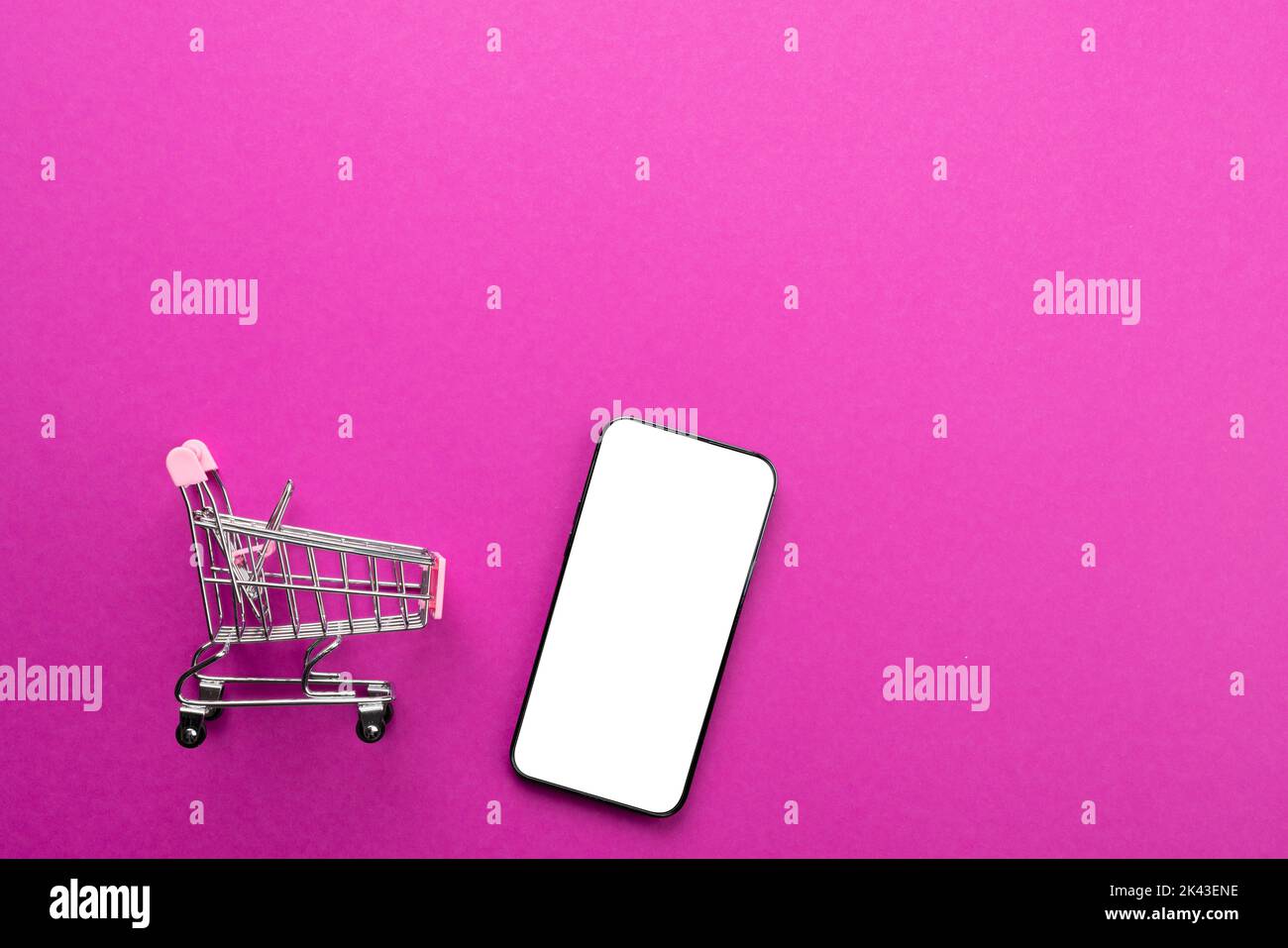 Composition of shopping cart and smartphone with copy space on pink ...