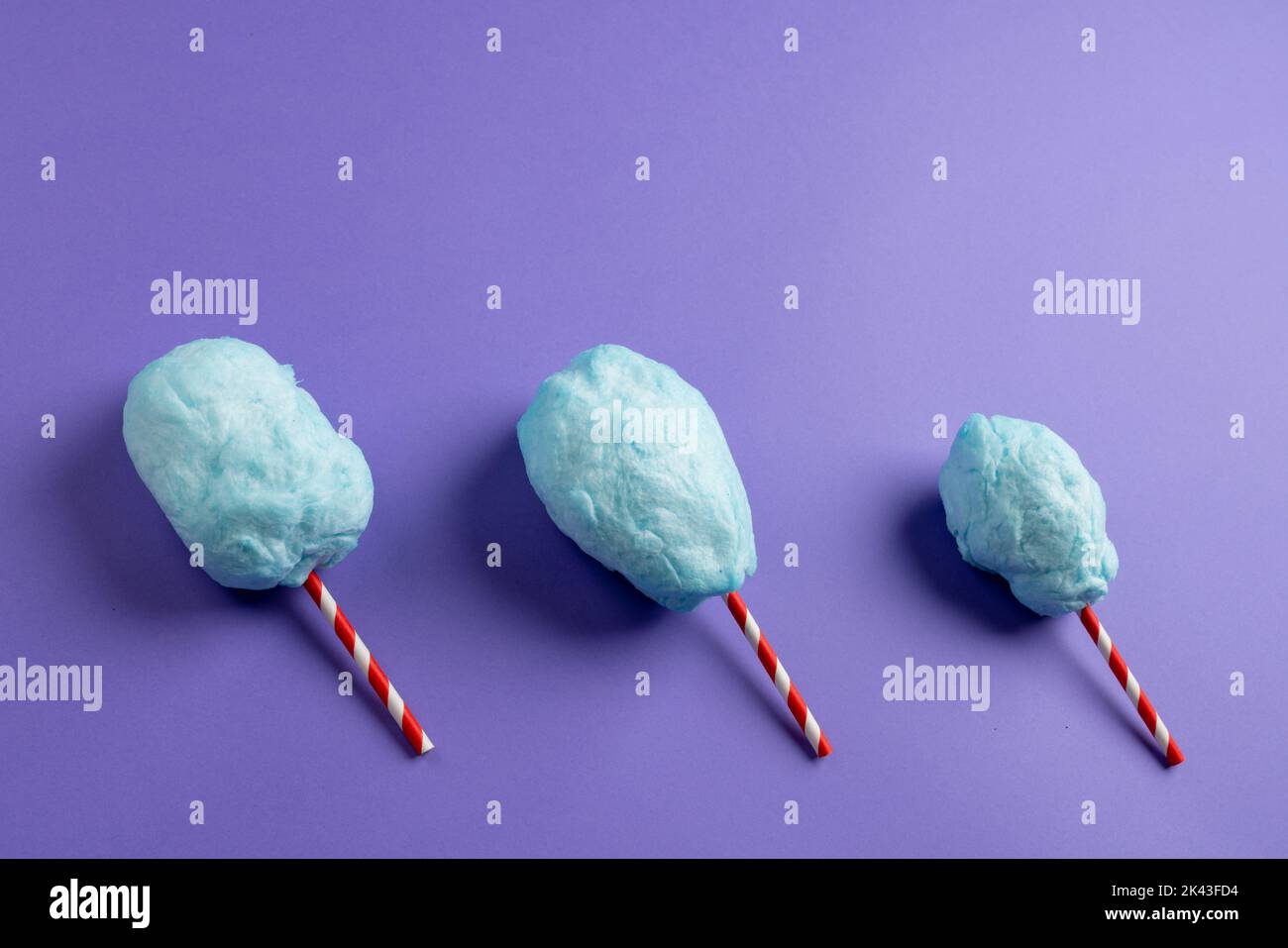 Horizontal image of homemade blue candy floss on three striped sticks, on purple with copy space Stock Photo