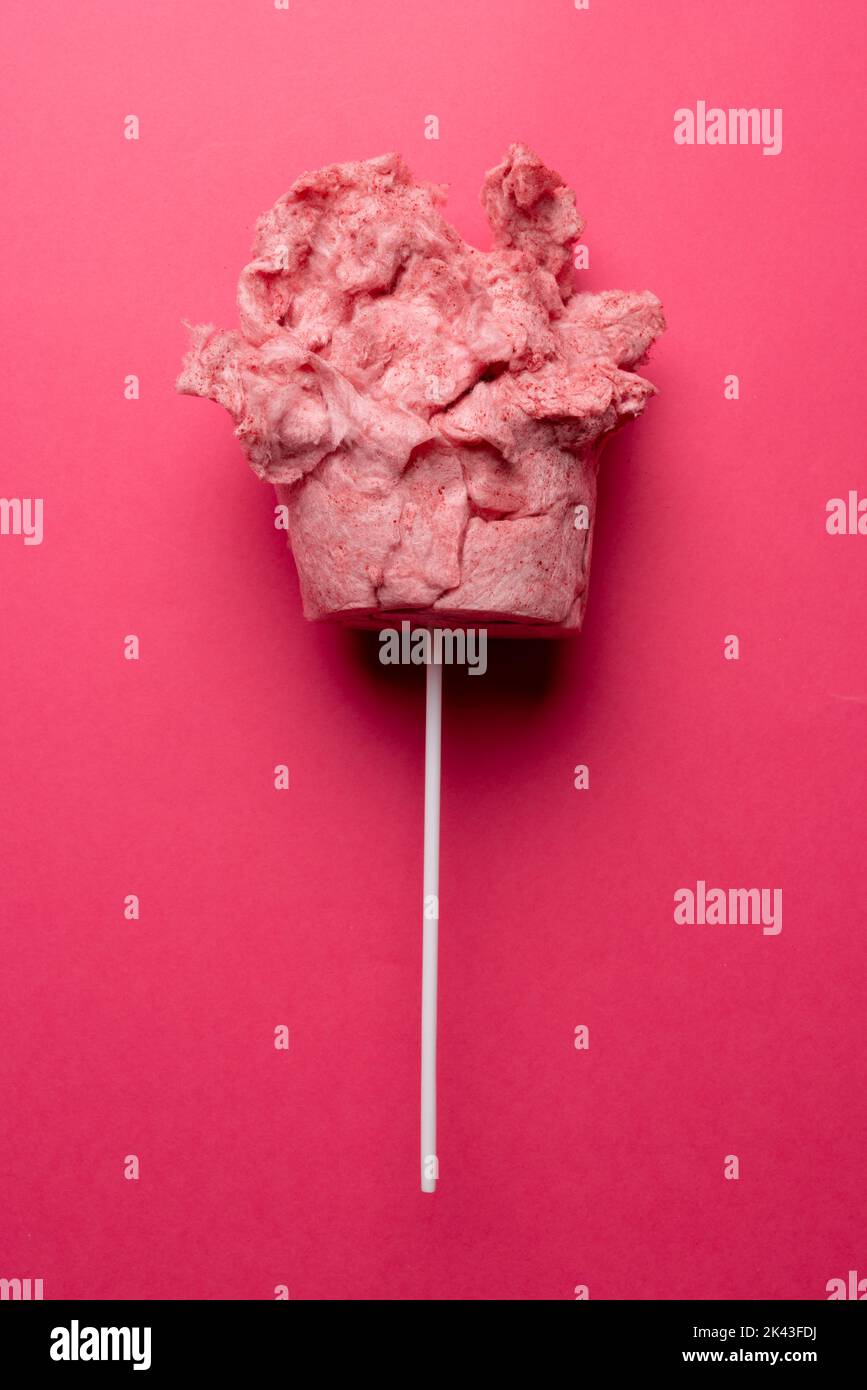 Vertical image of homemade pink candy floss on stick, on pink