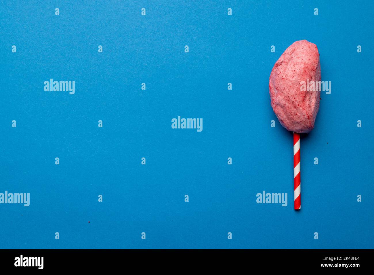 Horizontal image of homemade pink candy floss on striped stick, on blue