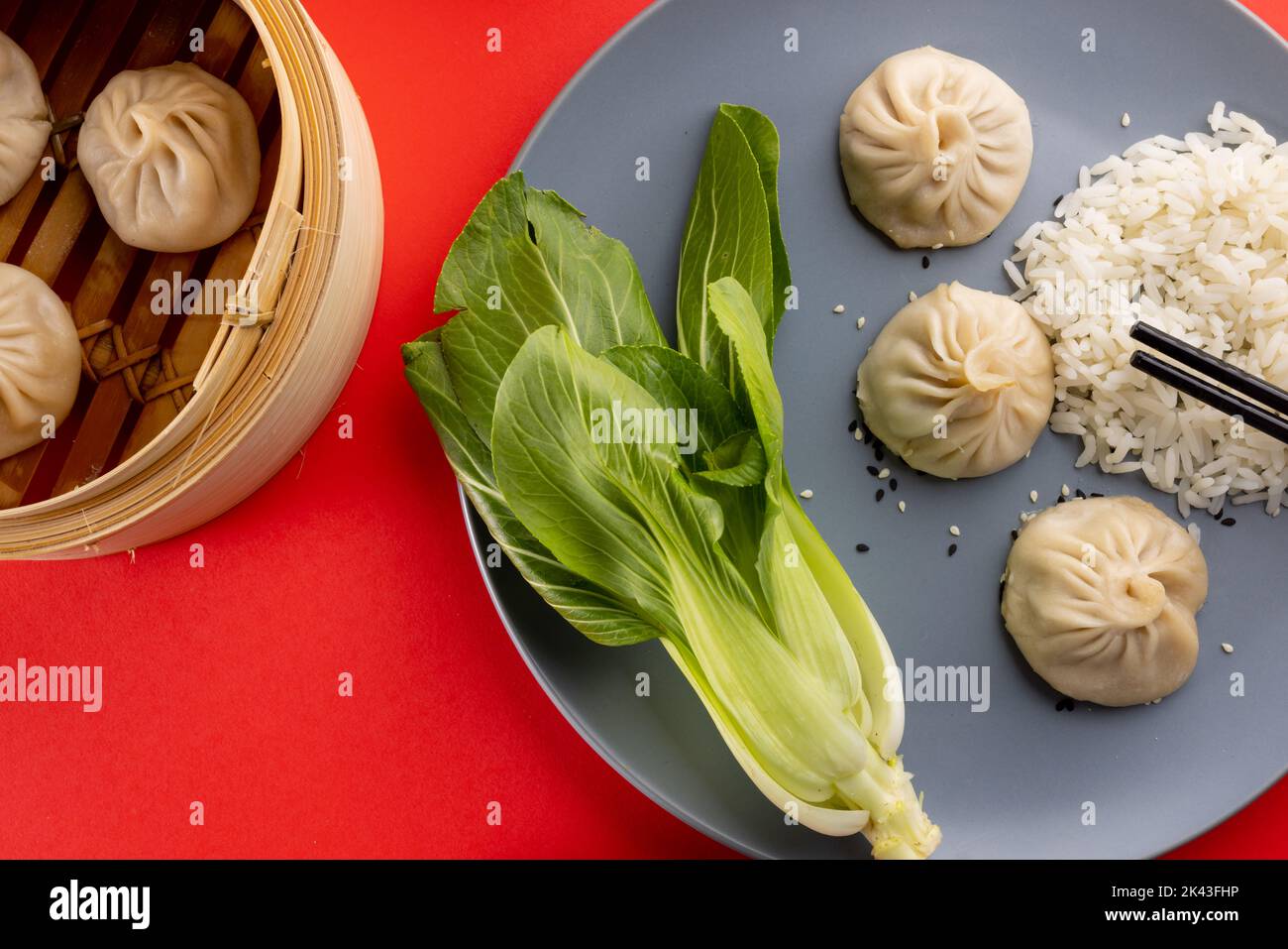 Overhead view of asian dumplings, rice, endive and chopsticks on red background Stock Photo
