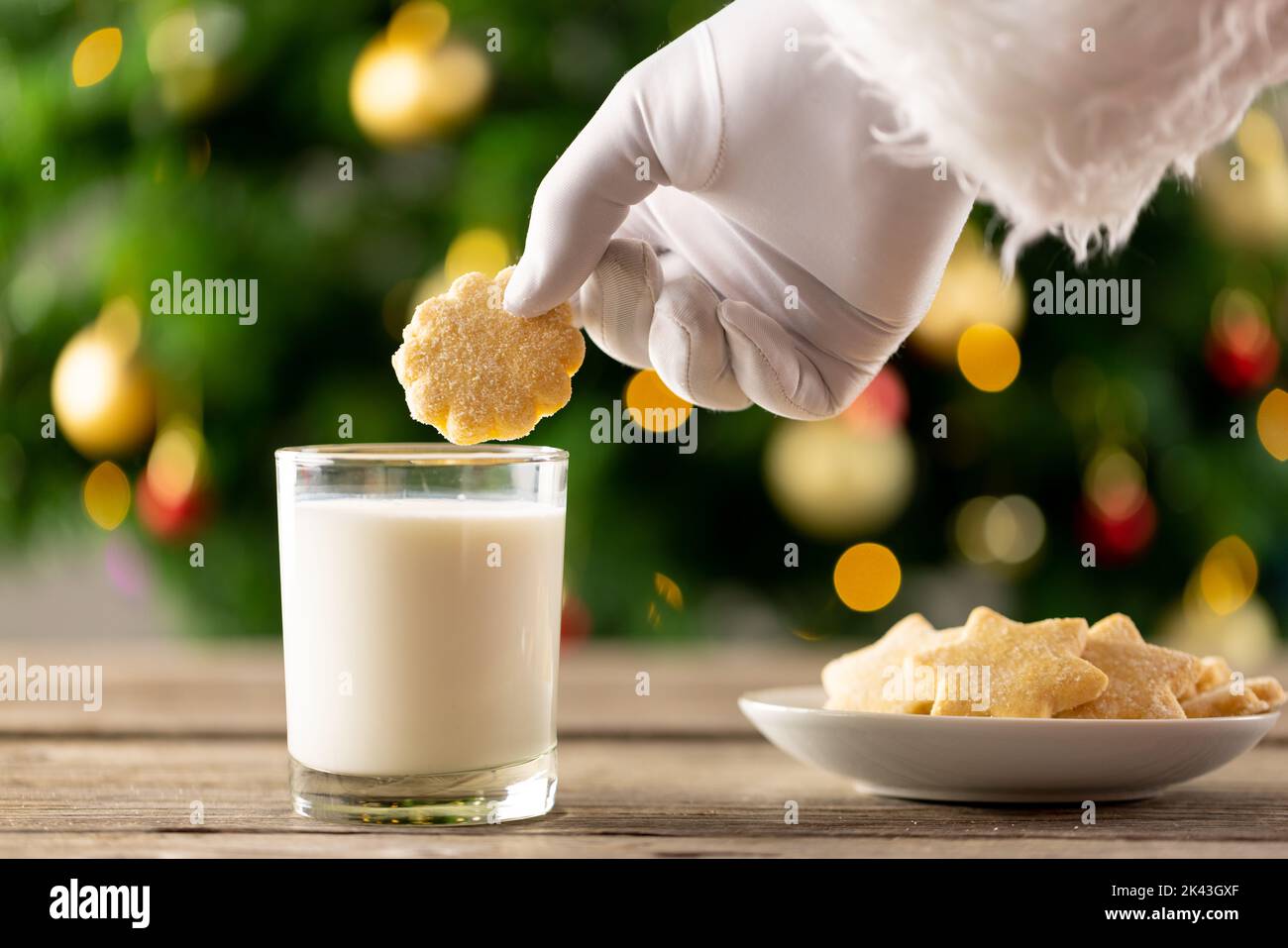 Image of hand of santa claus holding christmas biscuit over glass of milk Stock Photo