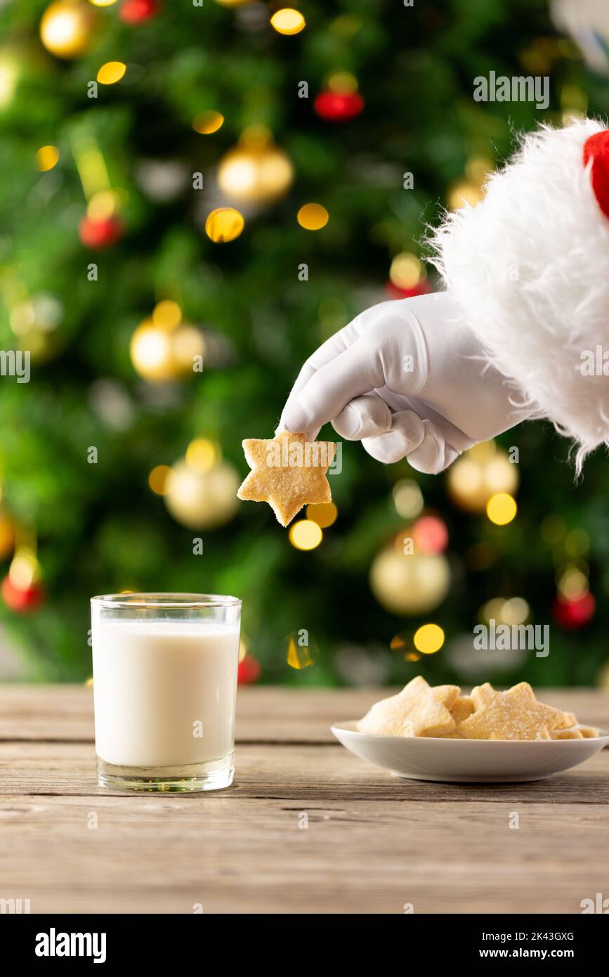 Image of hand of santa claus holding christmas star biscuit over glass of milk Stock Photo