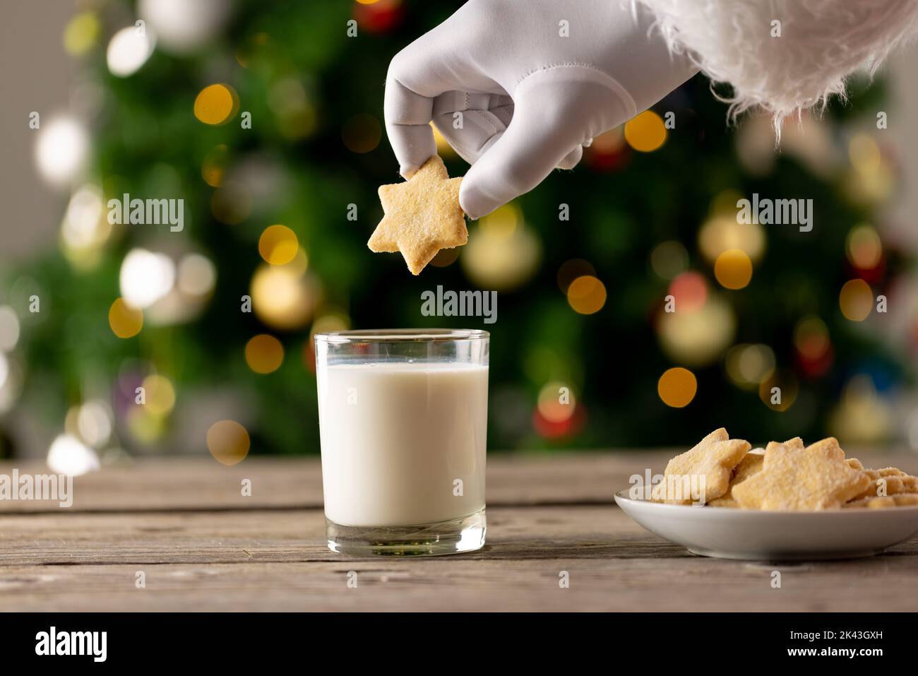 Image of hand of santa claus holding christmas star biscuit over glass of milk Stock Photo