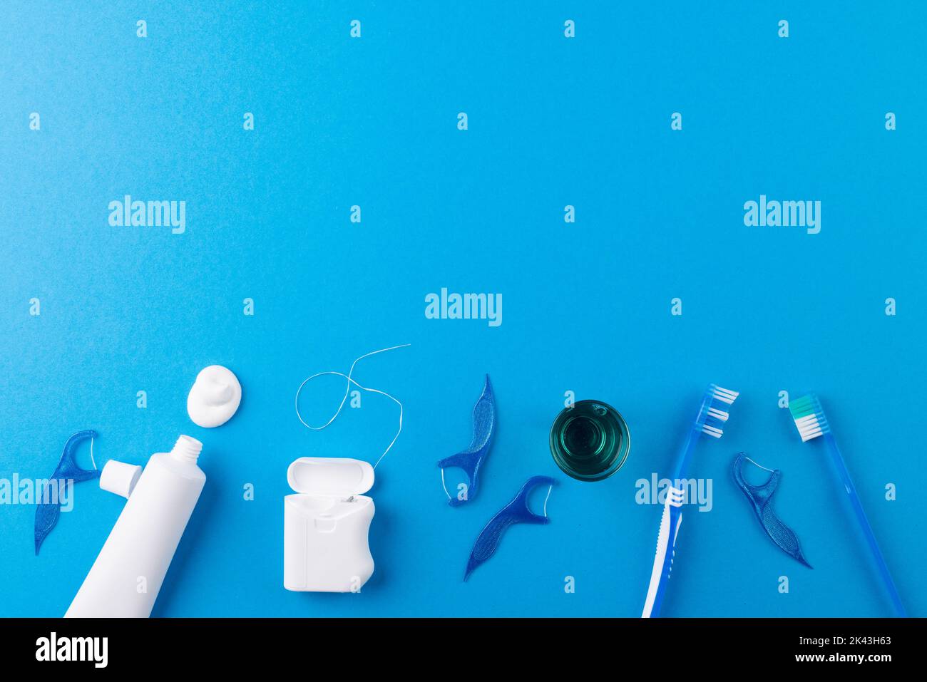 Image of toothbrush, toothpaste, string and liquid on blue surface