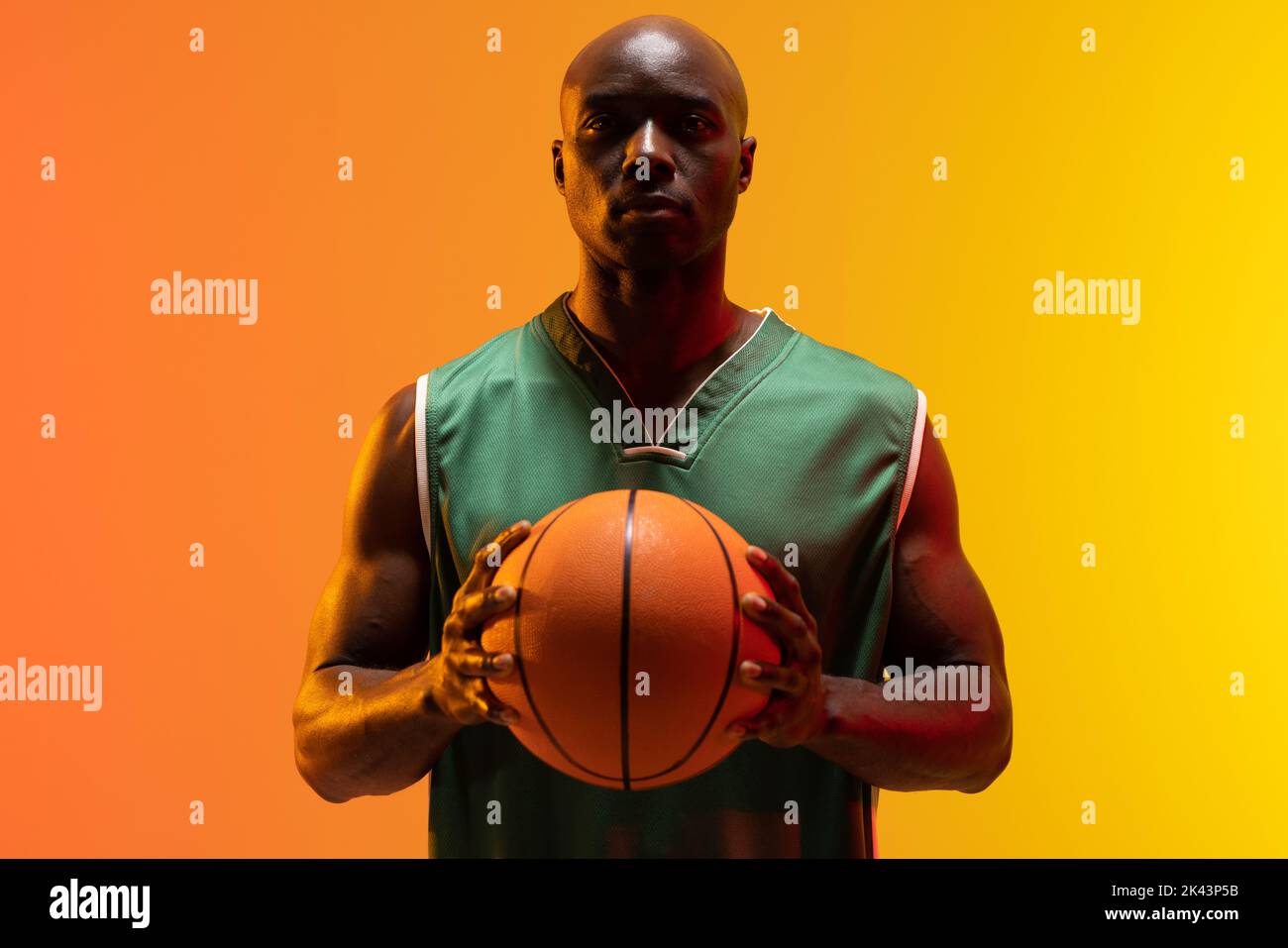 Image of portrait of african american basketball player with basketball on neon orange background. Sports and competition concept. Stock Photo