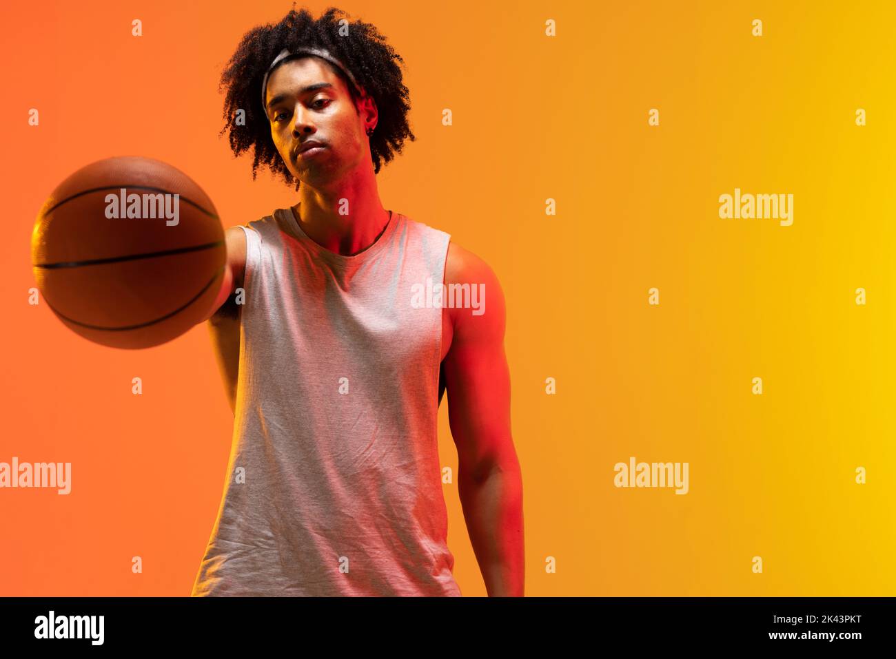 Image of biracial basketball player with basketball on orange to yellow background. Sports and competition concept. Stock Photo