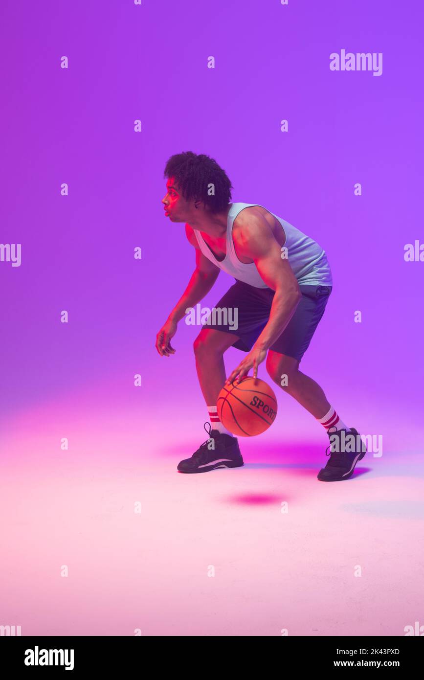 Image of biracial basketball player bouncing basketball on neon purple