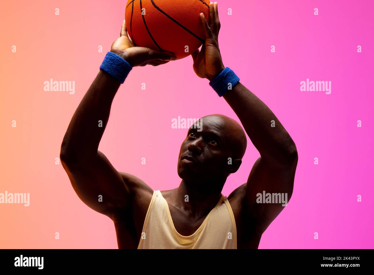 Image of african american basketball player throwing basketball on orange to pink background. Sports and competition concept. Stock Photo